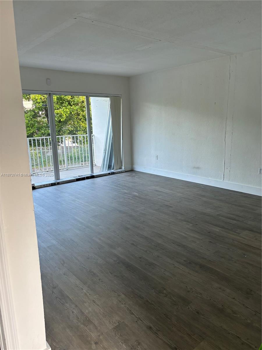 An empty room features wood-look flooring, white walls, and a sliding glass door to a balcony — 7701 SW 88th St # B224, Miami FL 33156, MIAMI, FL