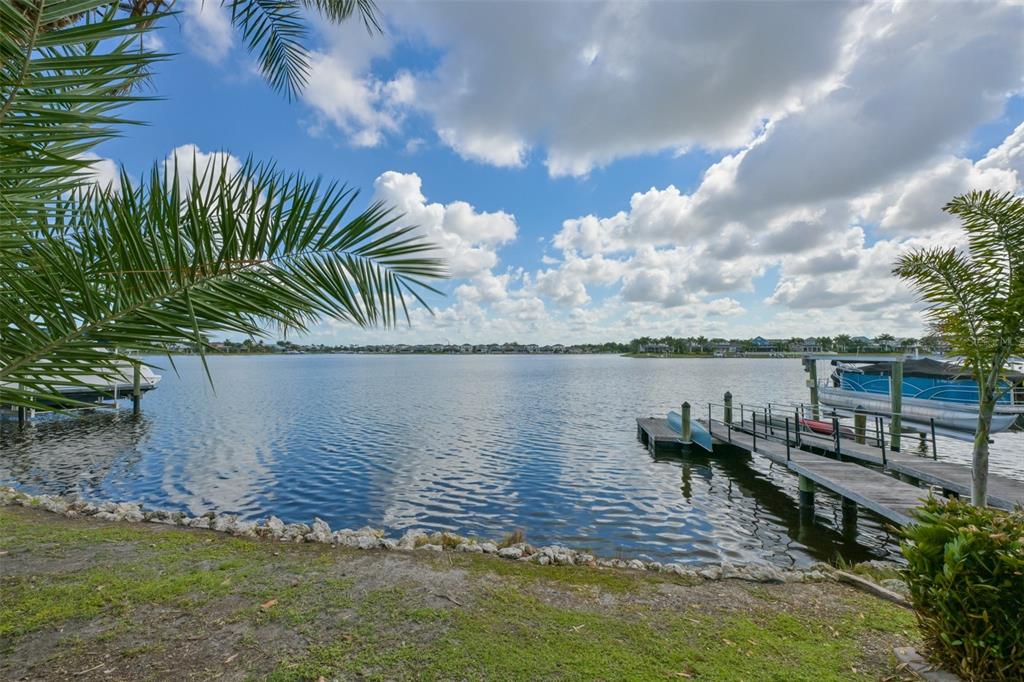 A view of a lake with a wooden dock, a boat, and palm trees — 5229 BRIGHTON SHORE DRIVE, APOLLO BEACH, FL