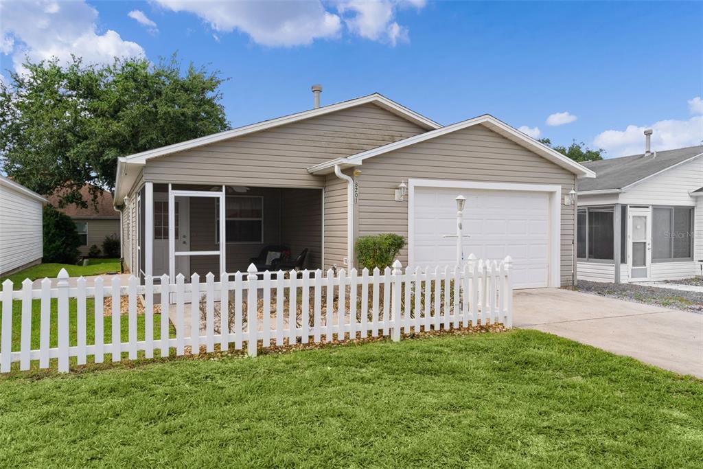 A tan, single-story house with a white picket fence, a screened porch, and a garage — 8201 SE 169TH PALOWNIA LOOP, THE VILLAGES, FL