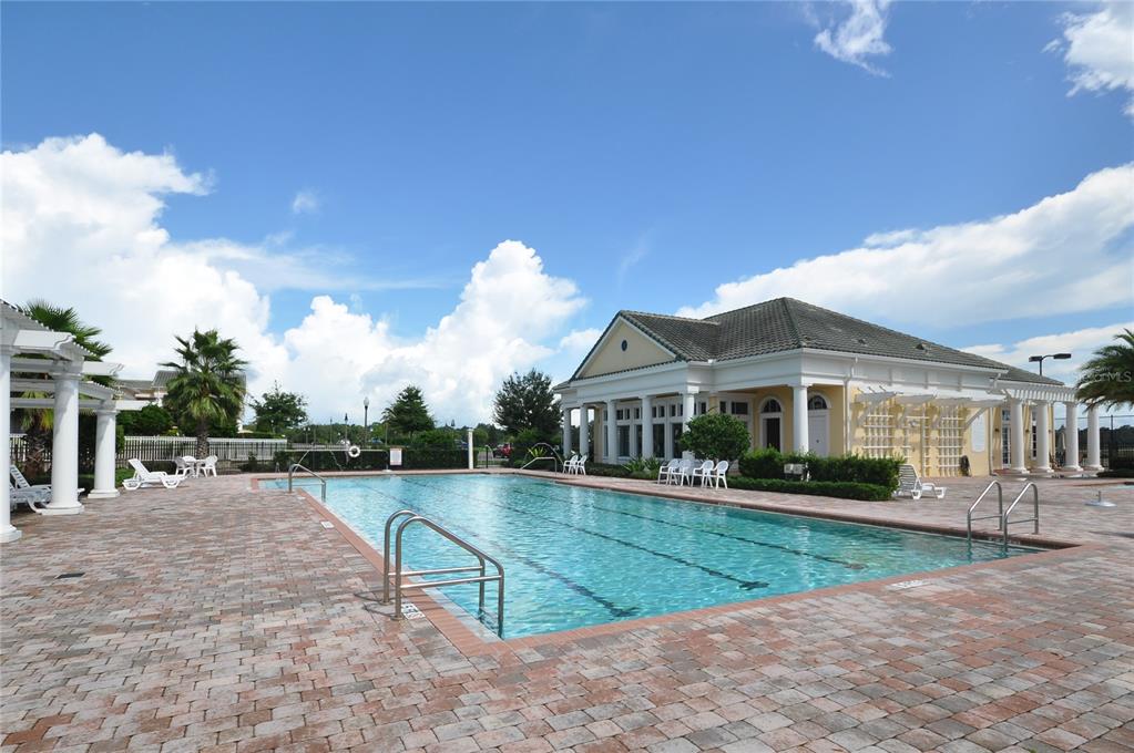 A rectangular swimming pool sits on a brick patio in front of a clubhouse building — 5558 LEWISHAM DRIVE, DAVENPORT, FL