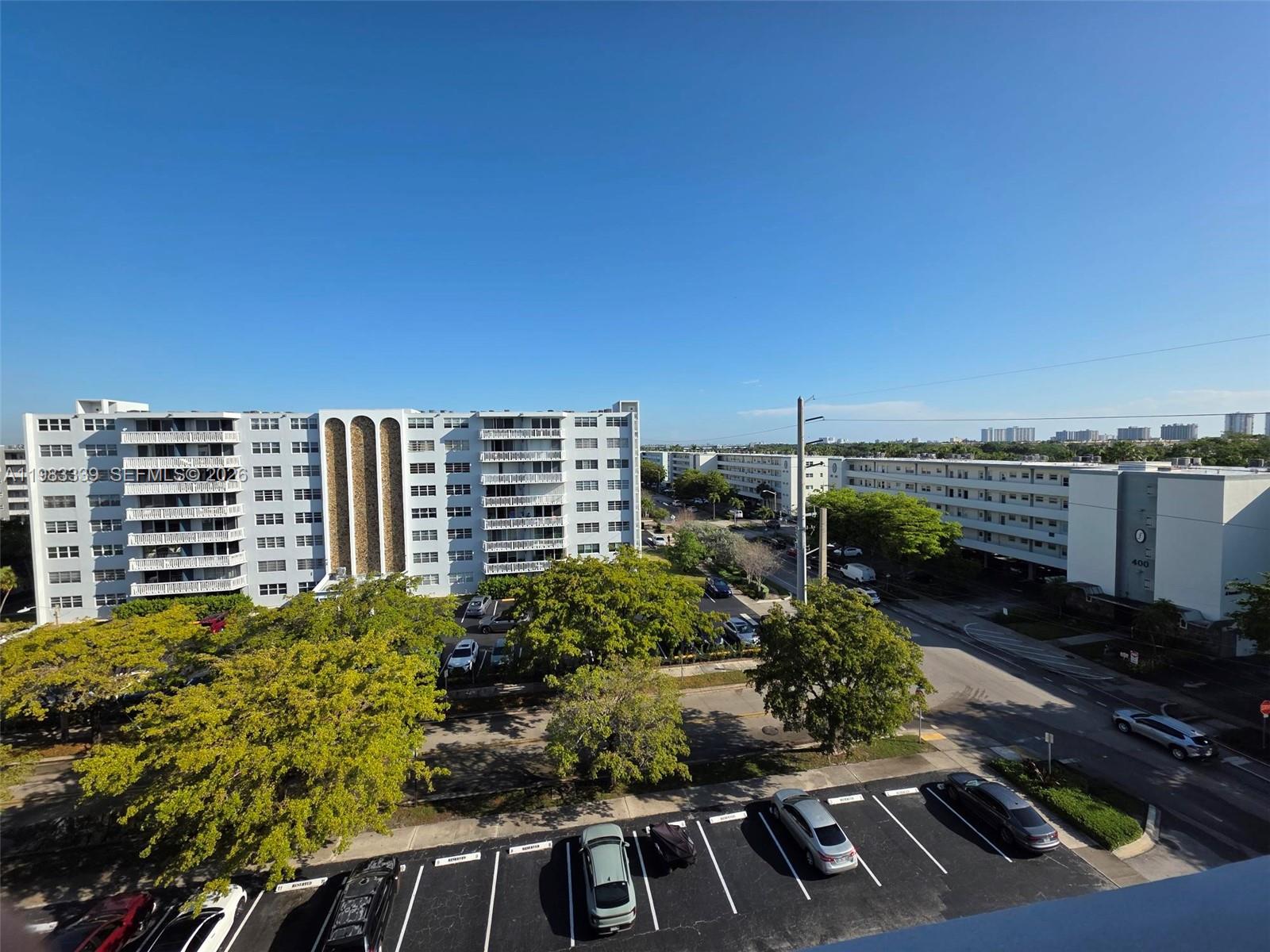 An elevated view of apartment buildings, parking lots, and trees under a clear blue sky — 319 NE 14th Ave # 702, Hallandale Beach FL 33009, HALLANDALE BEACH, FL