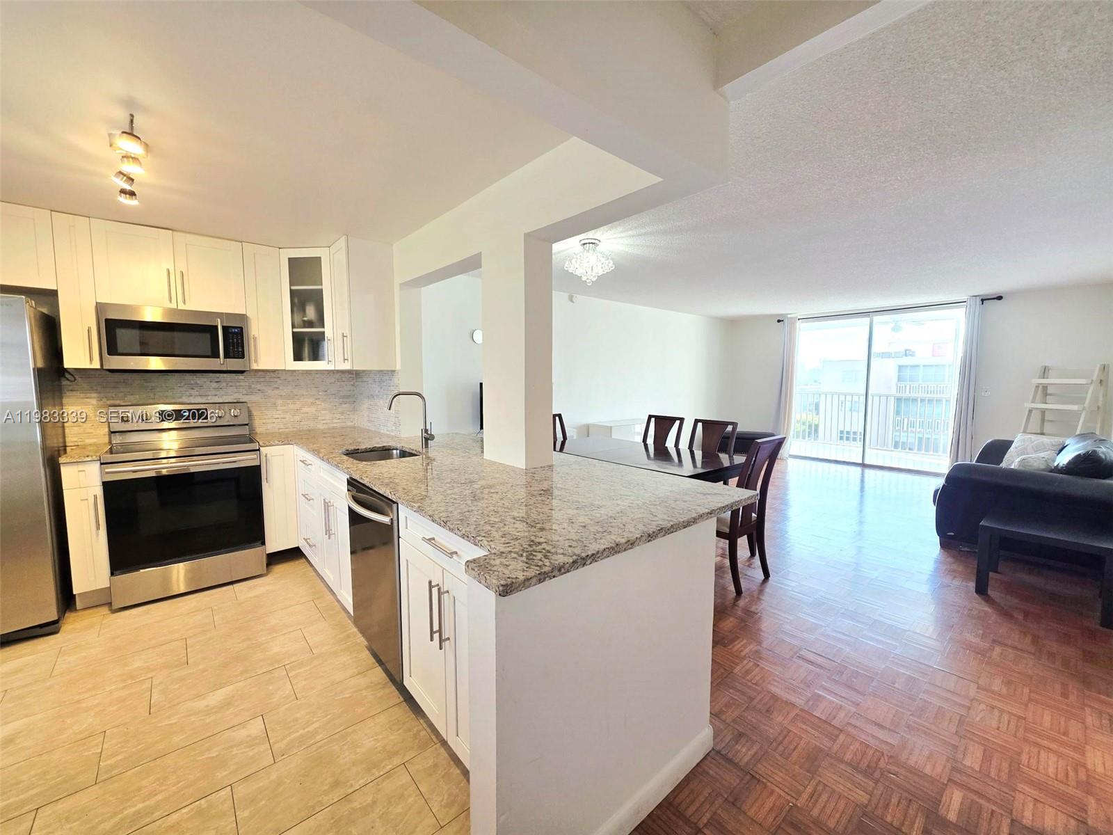 A kitchen with granite countertops and white cabinets opens into a living and dining area — 319 NE 14th Ave # 702, Hallandale Beach FL 33009, HALLANDALE BEACH, FL