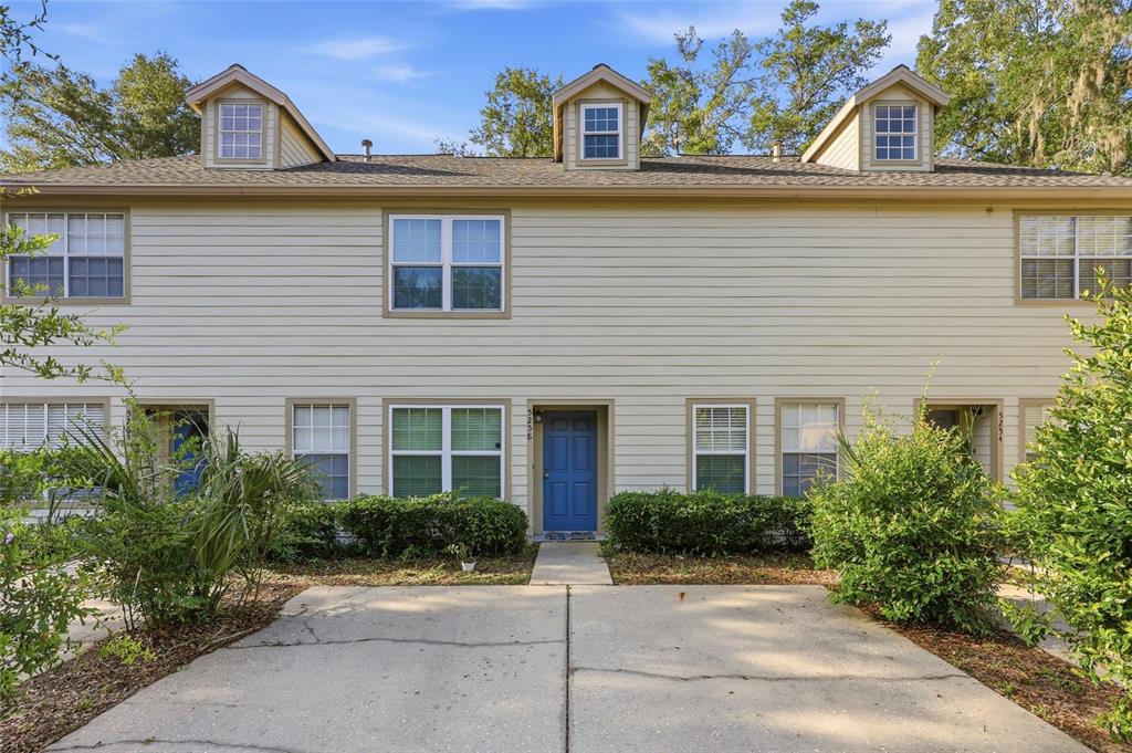 A two-story townhouse exterior with light siding, a blue front door, and three dormer windows — 5258 SW 97TH DRIVE, GAINESVILLE, FL