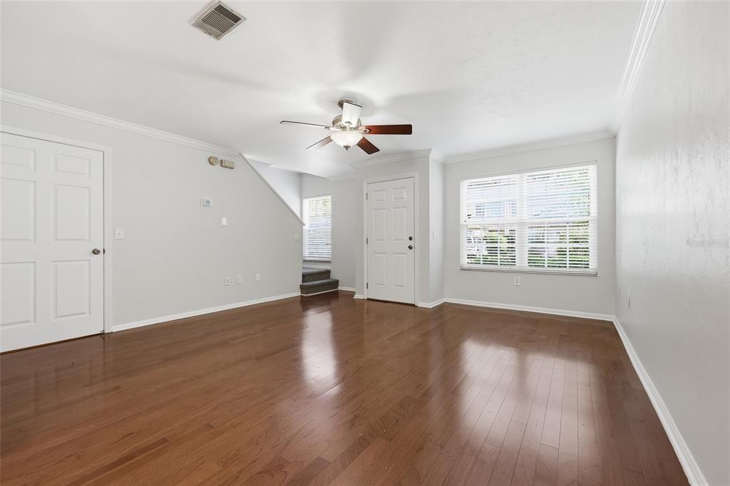 An empty room with hardwood floors, a ceiling fan, white walls, and a staircase — 5258 SW 97TH DRIVE, GAINESVILLE, FL