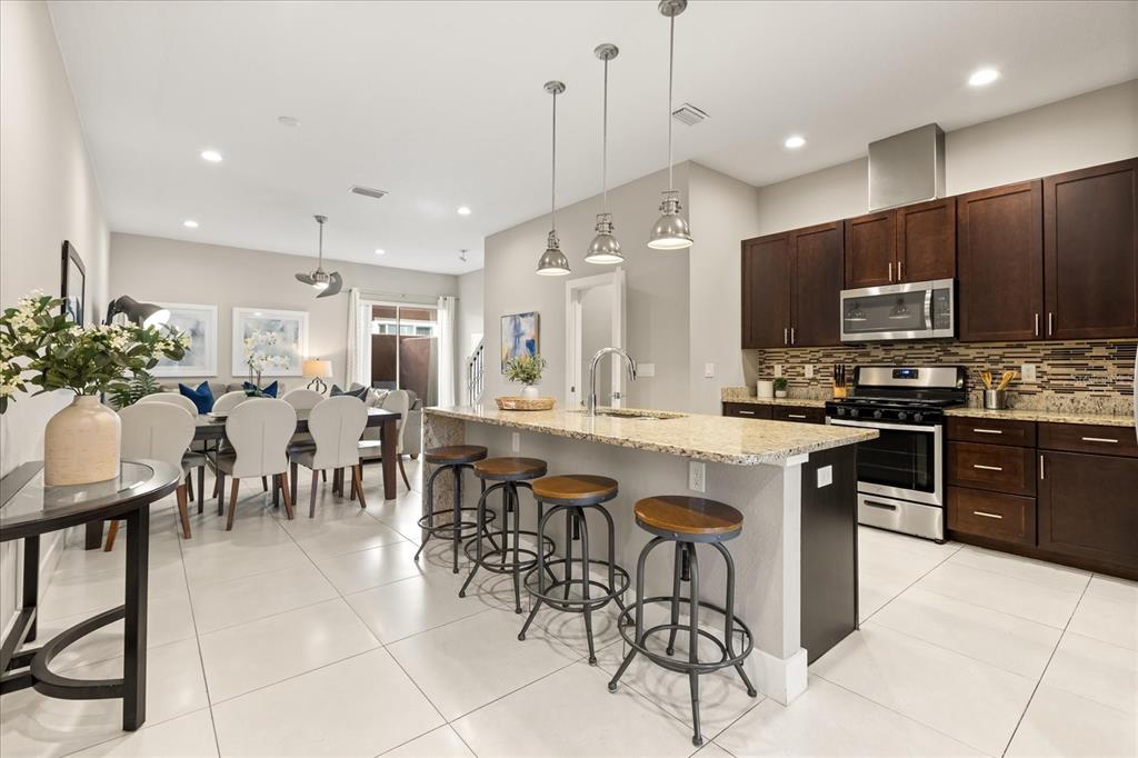 A kitchen with dark wood cabinets, stainless steel appliances, granite countertops, and a tiled backsplash — 2637 SUNRISE SHORES DRIVE, KISSIMMEE, FL