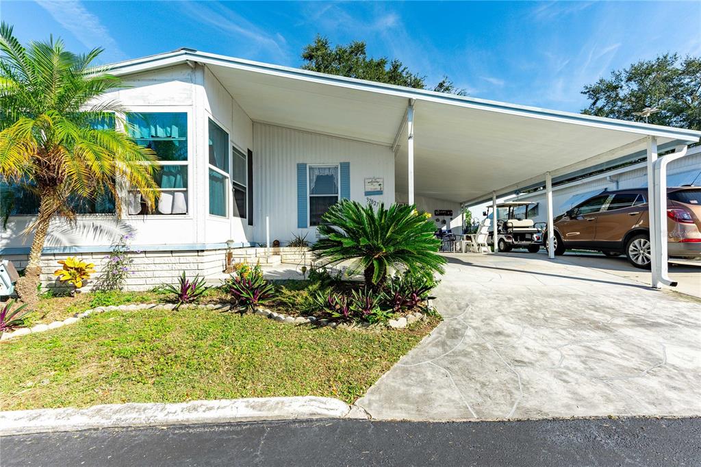 A white manufactured home features a carport, a golf cart, and a paved driveway — 37827 MISSION HILLS AVENUE, ZEPHYRHILLS, FL