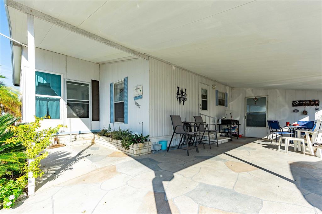 A covered concrete patio features outdoor furniture and a white exterior wall with windows — 37827 MISSION HILLS AVENUE, ZEPHYRHILLS, FL