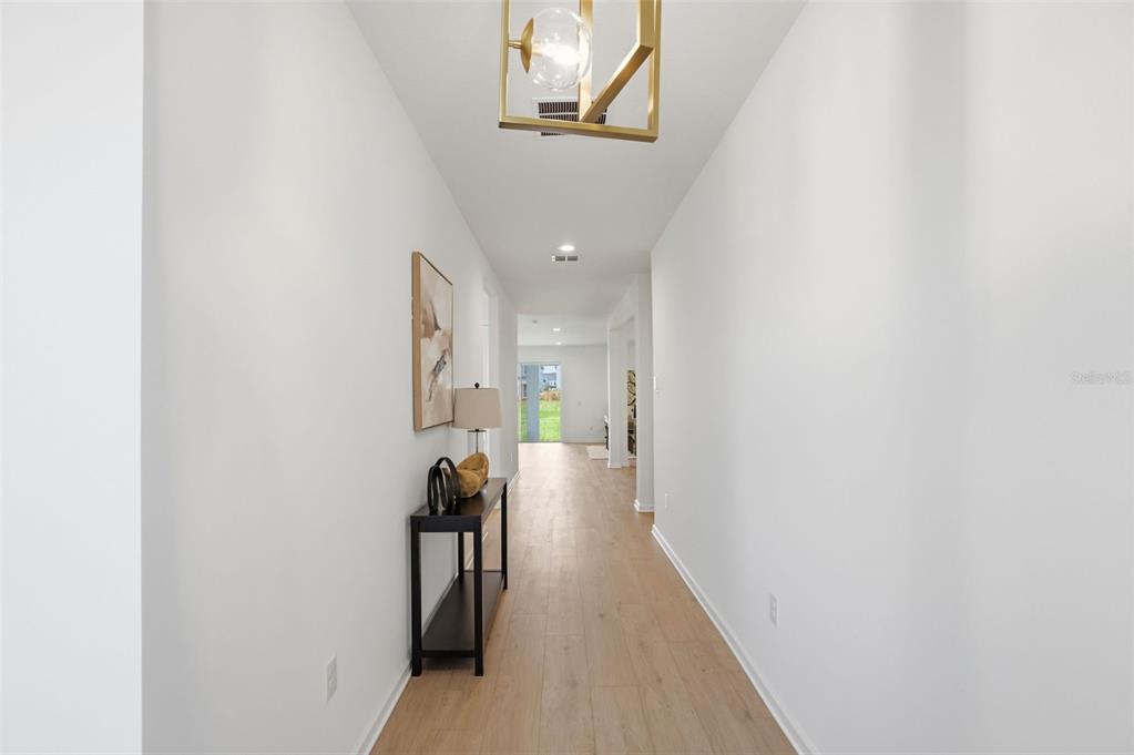 A long hallway features light wood-look flooring, white walls, and a modern gold pendant light — 1595 STONECLIFFF DRIVE, APOPKA, FL