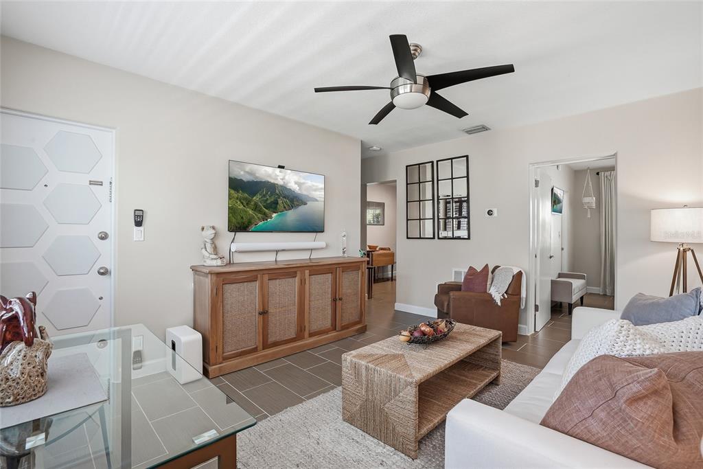 A living room features a wall-mounted television, a wooden media console, and a ceiling fan — 410 12TH AVENUE NE UNIT 8, ST PETERSBURG, FL