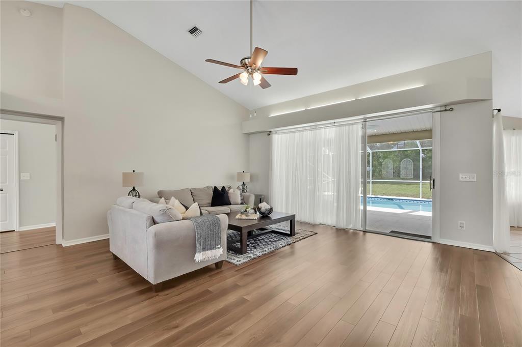A living room with light wood floors, a vaulted ceiling, and sliding glass doors to a pool — 13290 DON LOOP, SPRING HILL, FL