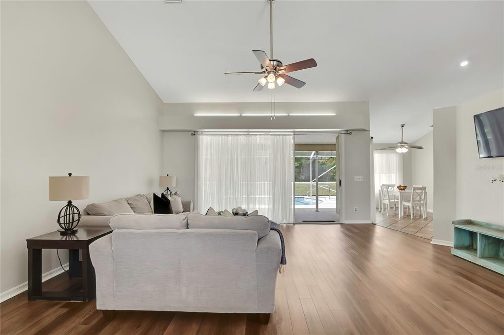 A living room with wood-look flooring, a ceiling fan, and a view of a pool — 13290 DON LOOP, SPRING HILL, FL