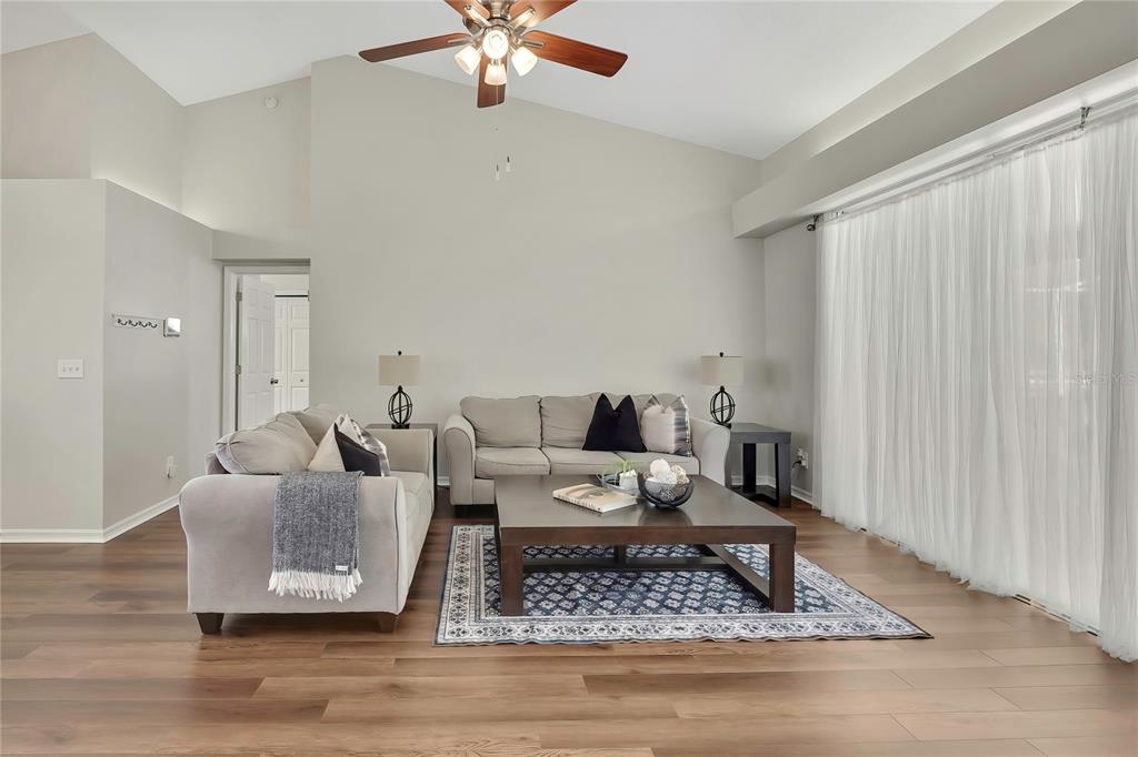 A living room features a vaulted ceiling, wood-look flooring, two sofas, and a large window — 13290 DON LOOP, SPRING HILL, FL