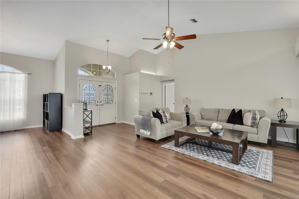 A living room features light walls, wood-look flooring, a vaulted ceiling, and double front doors — 13290 DON LOOP, SPRING HILL, FL