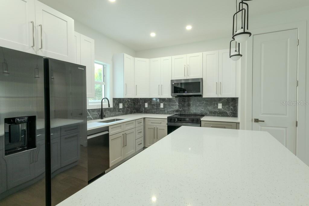 A modern kitchen features white cabinets, a large quartz island, and a dark marble backsplash — 4323 LA FRANCE AVENUE, NORTH PORT, FL