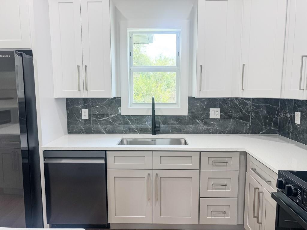 A kitchen features white upper cabinets, light gray lower cabinets, and a dark marble backsplash — 4323 LA FRANCE AVENUE, NORTH PORT, FL