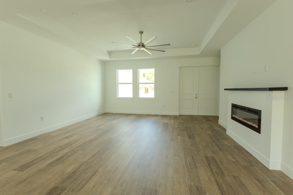 A living room features light wood-look flooring, a ceiling fan, and a wall-mounted fireplace — 4323 LA FRANCE AVENUE, NORTH PORT, FL