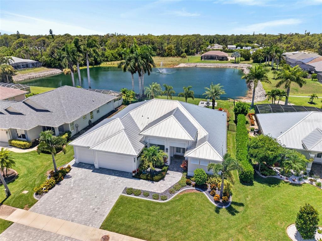 An aerial view shows a single-story house with a metal roof, driveway, and backyard pond — 28116 N MCCALL ROAD, ENGLEWOOD, FL