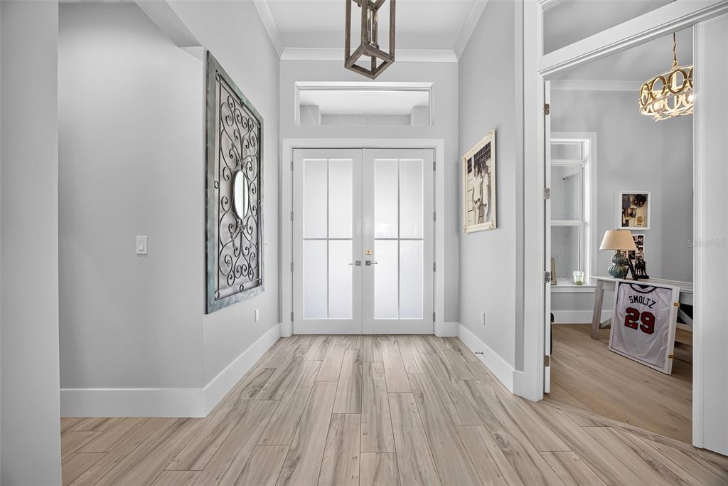 A bright entryway features light wood-look tile flooring, double glass doors, and a decorative wall mirror — 28116 N MCCALL ROAD, ENGLEWOOD, FL