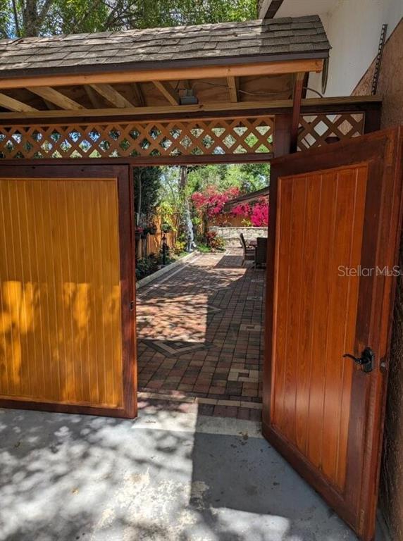 A wooden gate opens to a brick-paved patio area with lush landscaping and outdoor seating — 1602 AMBERLEA DRIVE S, DUNEDIN, FL