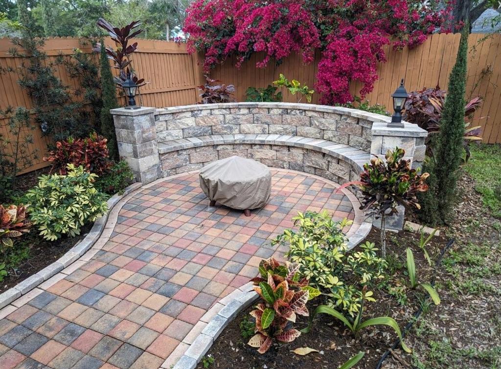 A curved stone bench and fire pit sit on a paver patio in a backyard — 1602 AMBERLEA DRIVE S, DUNEDIN, FL