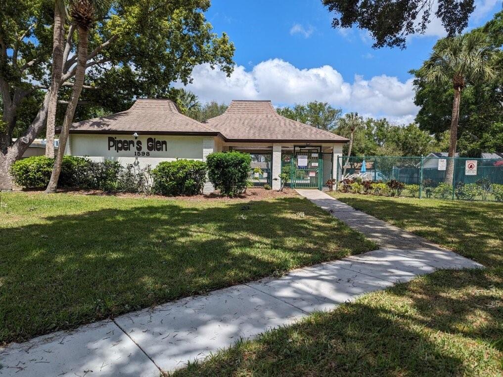 A single-story building with a brown roof and a gated entrance to a pool area — 1602 AMBERLEA DRIVE S, DUNEDIN, FL
