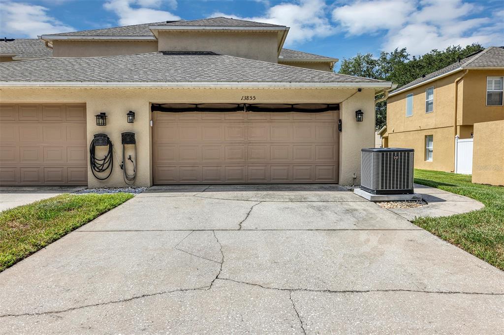 A beige two-car garage with a cracked concrete driveway and an outdoor air conditioning unit — 13855 GOLDEN RUSSET DRIVE, WINTER GARDEN, FL