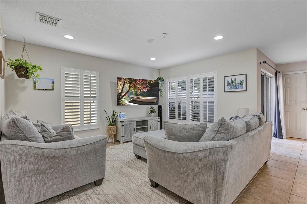 A living room features light gray sofas, a television, plantation shutters, and tile flooring — 13855 GOLDEN RUSSET DRIVE, WINTER GARDEN, FL