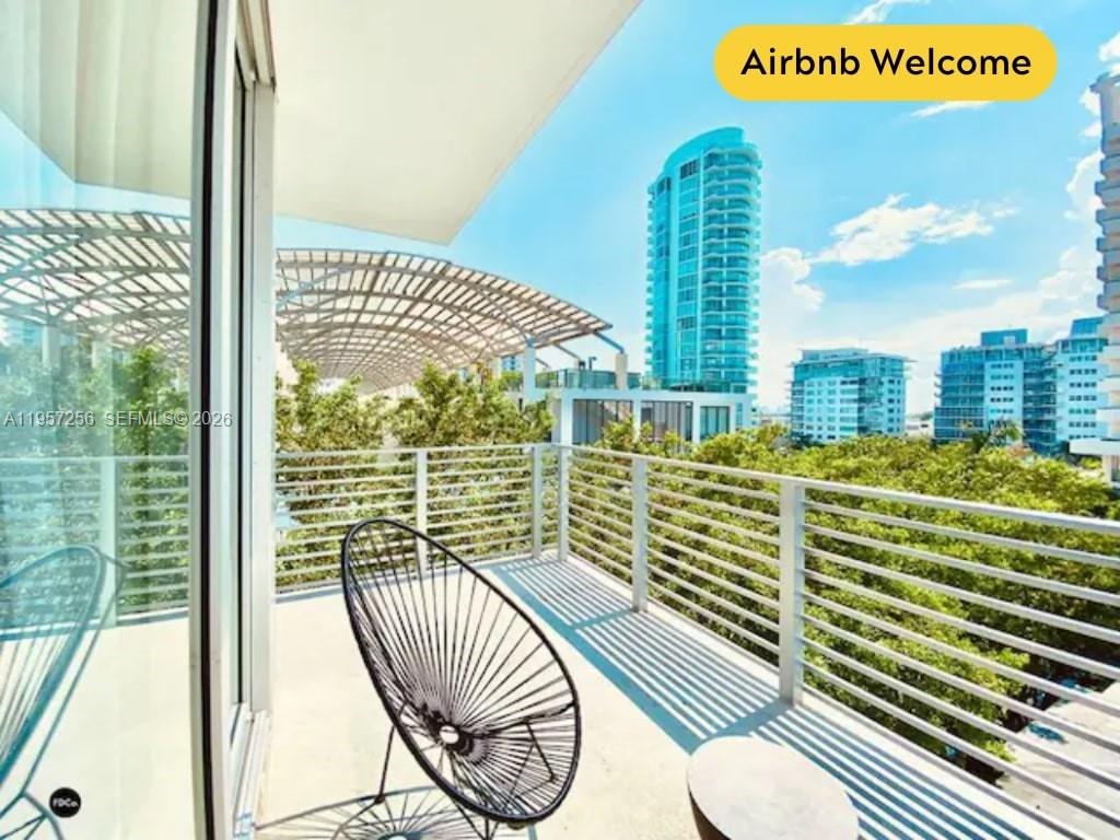 A balcony with a modern chair overlooks a city skyline with tall buildings and trees — 6080 Collins Avenue, Miami Beach FL 33140, MIAMI BEACH, FL