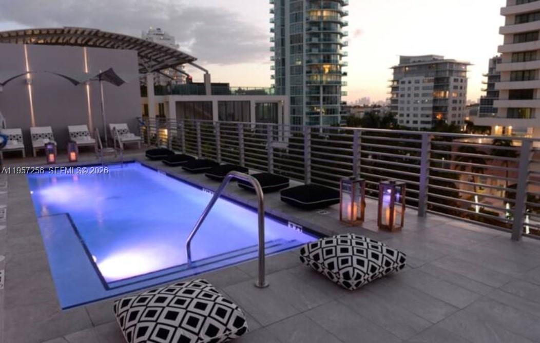 A rooftop swimming pool with lounge chairs and cushions overlooks a city skyline at dusk — 6080 Collins Avenue, Miami Beach FL 33140, MIAMI BEACH, FL