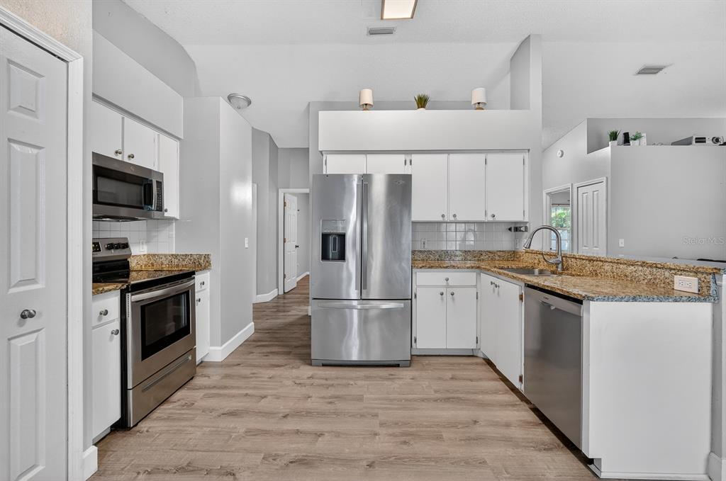 A kitchen features white cabinets, granite countertops, stainless steel appliances, and wood-look flooring — 3639 OLD HAMMOCK ROAD, PORT ORANGE, FL