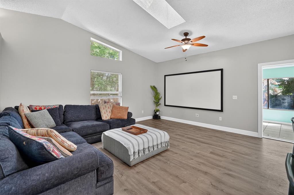 A living room features a large projection screen, a dark sectional sofa, and wood-look flooring — 3639 OLD HAMMOCK ROAD, PORT ORANGE, FL