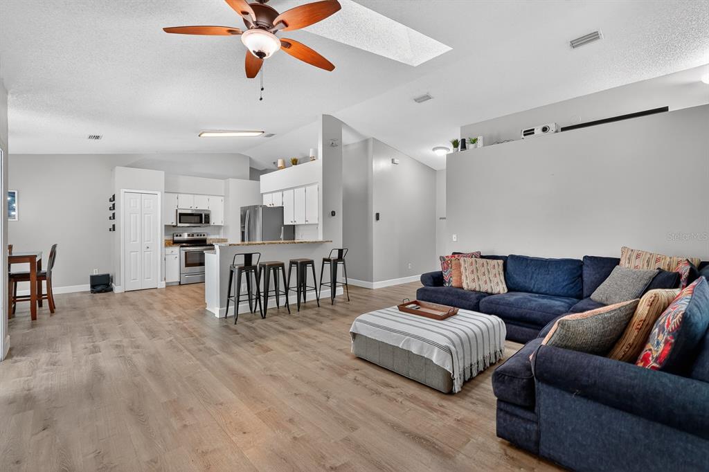 An open-concept living room features wood-look flooring, a blue sectional sofa, and a kitchen island — 3639 OLD HAMMOCK ROAD, PORT ORANGE, FL