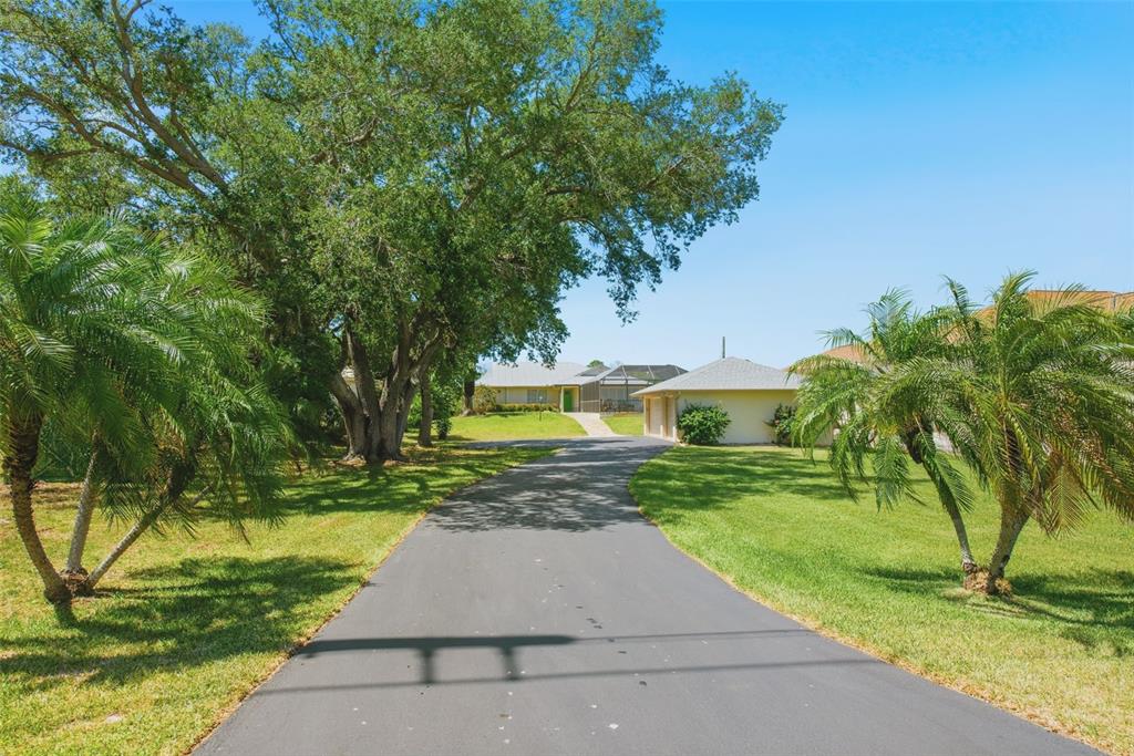 A long asphalt driveway leads to a house with a screened pool enclosure and trees — 880 LEMON BAY DRIVE, VENICE, FL