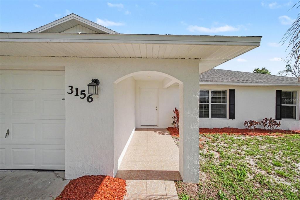 A white stucco house exterior features a covered entryway, a garage, and a tiled walkway — 3156 COVENTRY STREET, DELTONA, FL