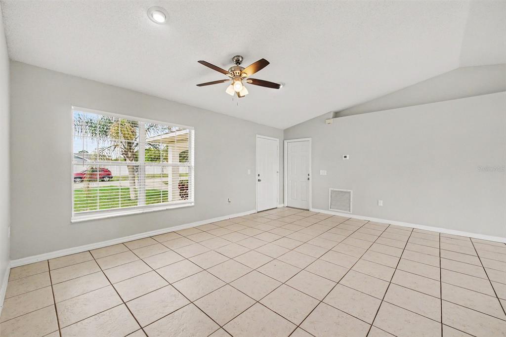 A bright, empty room features light-colored tile flooring, a ceiling fan, and a large window — 3156 COVENTRY STREET, DELTONA, FL