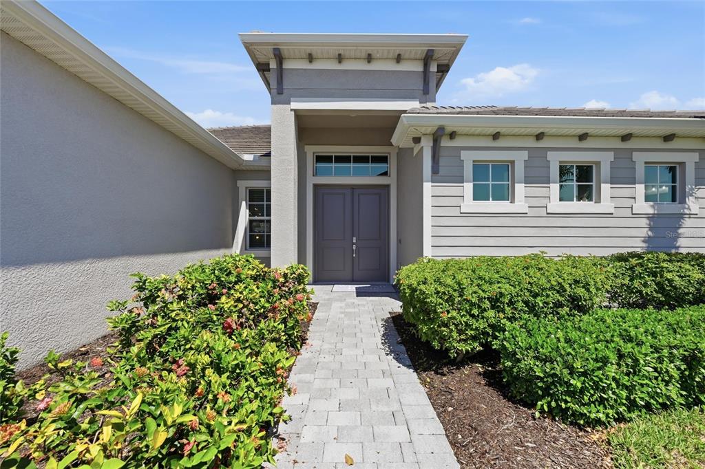 A paved walkway leads to the double front doors of a house with gray siding — 17139 JADESTONE COURT, VENICE, FL