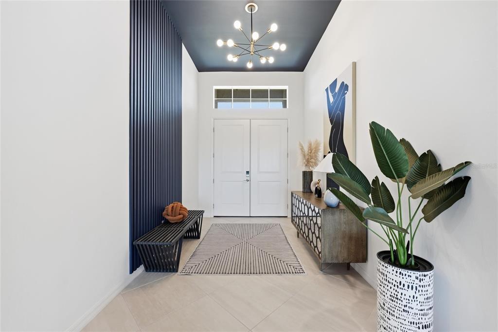 A modern entryway features a dark blue slatted accent wall, a chandelier, and double doors — 17139 JADESTONE COURT, VENICE, FL