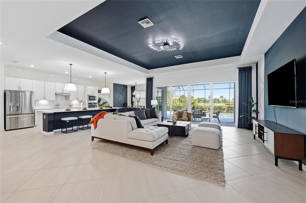 An open-concept living room and kitchen feature a dark blue tray ceiling and tile flooring — 17139 JADESTONE COURT, VENICE, FL