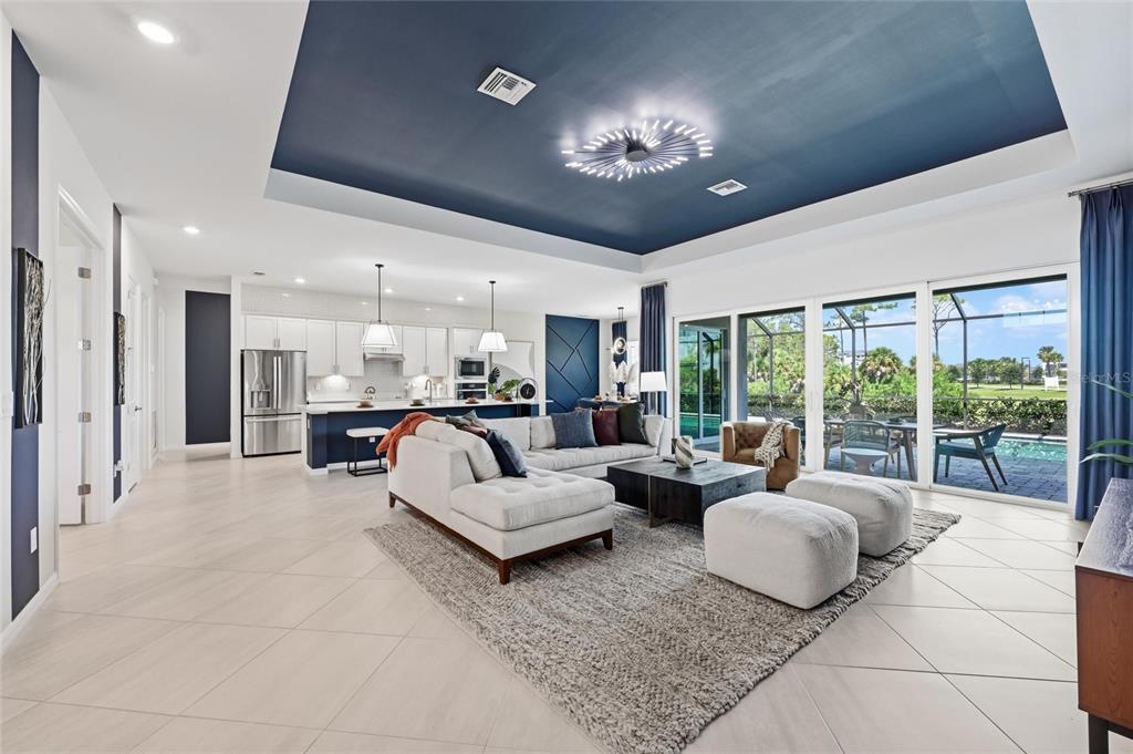 An open-concept living room and kitchen feature a navy tray ceiling and sliding glass doors — 17139 JADESTONE COURT, VENICE, FL