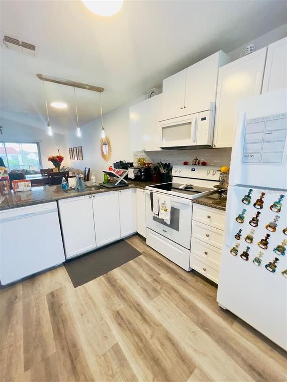 A kitchen with white cabinets, white appliances, granite countertops, and light wood-look flooring — 2500 WOODGATE BOULEVARD UNIT 203, ORLANDO, FL