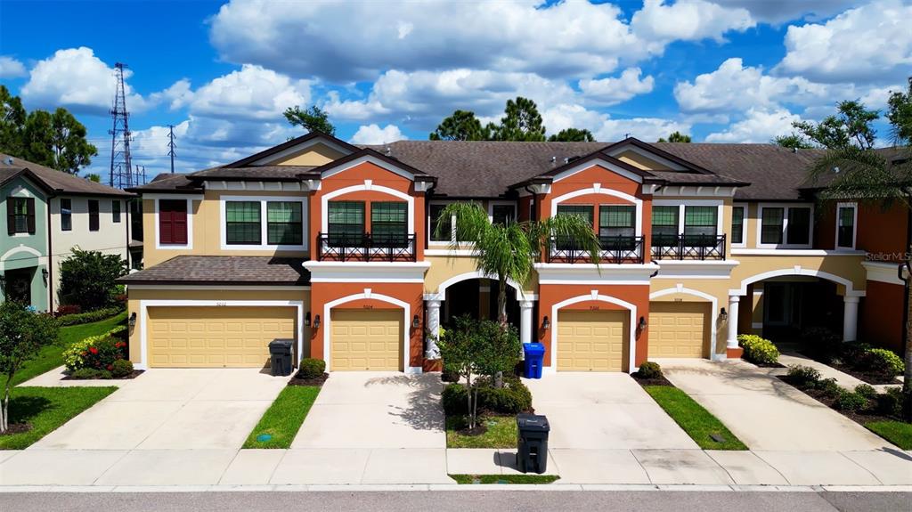 A multi-unit townhouse building features orange and beige stucco facades with attached garages — 9204 FOX SPARROW ROAD, TAMPA, FL