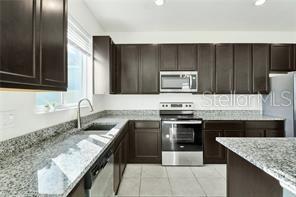 A kitchen features dark wood cabinets, granite countertops, and stainless steel appliances — 911 ALVANLEY COURT, DAVENPORT, FL