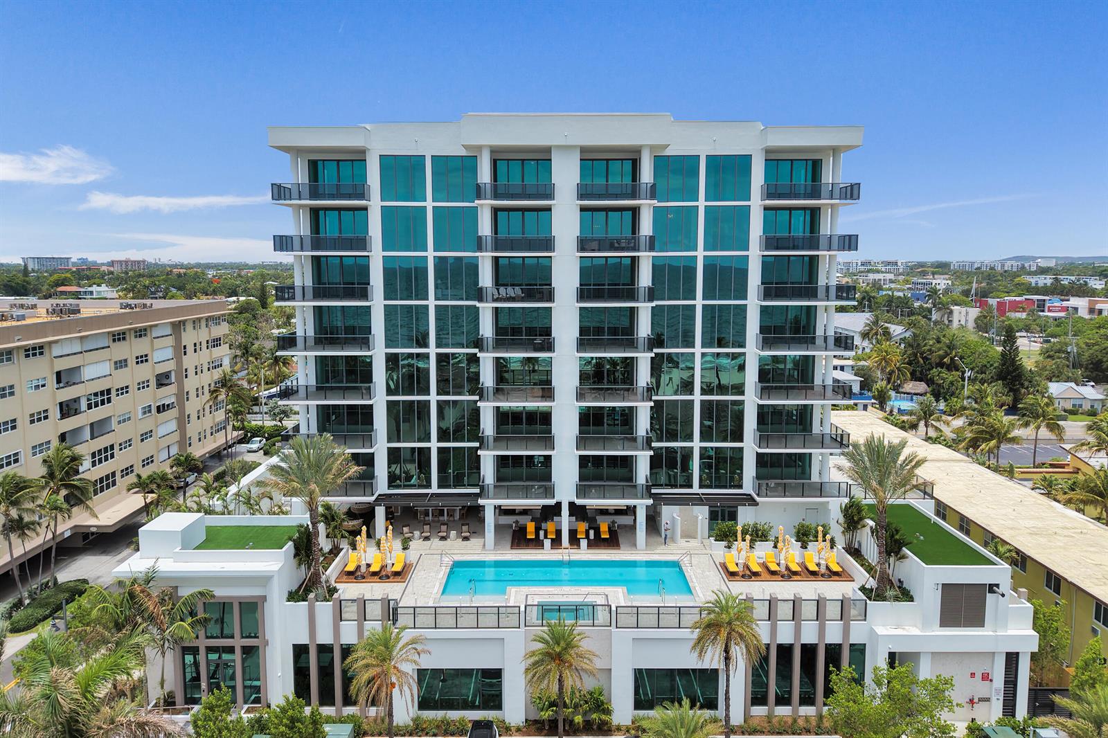 An aerial view of a modern multi-story apartment building with a ground-level swimming pool — 305 Briny Avenue # 306, Pompano Beach FL 33062, POMPANO BEACH, FL