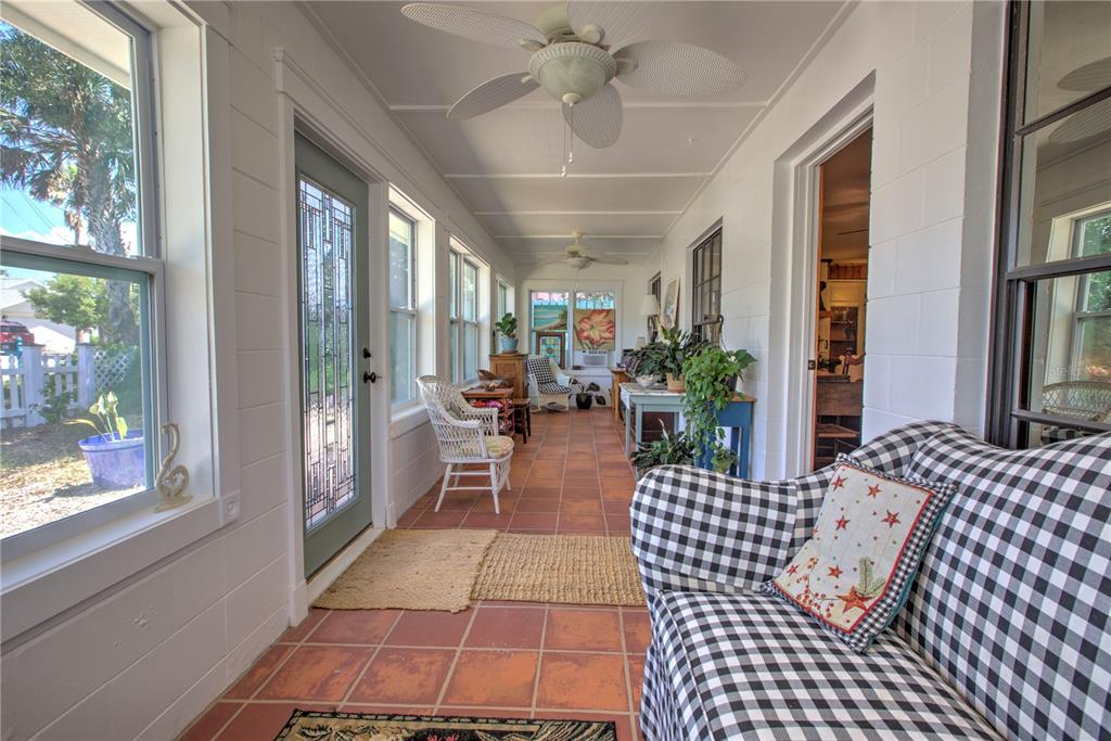 A sunroom features terracotta tile floors, white block walls, ceiling fans, and a checkered sofa — 825 E 23RD AVENUE, NEW SMYRNA BEACH, FL