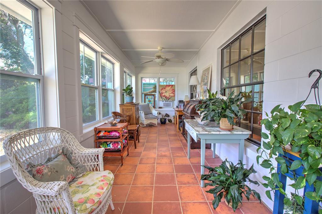 A sunroom features terracotta tile flooring, white paneled walls, large windows, and wicker furniture — 825 E 23RD AVENUE, NEW SMYRNA BEACH, FL