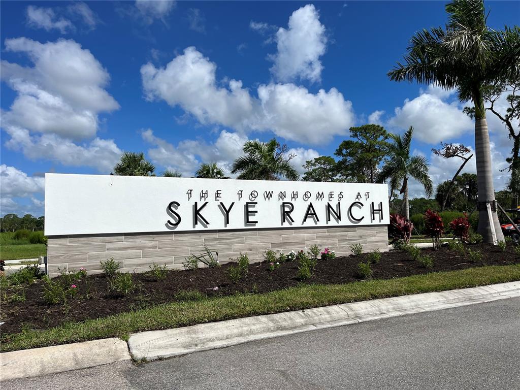 A white monument sign for The Townhomes at Skye Ranch stands beside a palm tree — 8500 LUNAR SKYE STREET, SARASOTA, FL