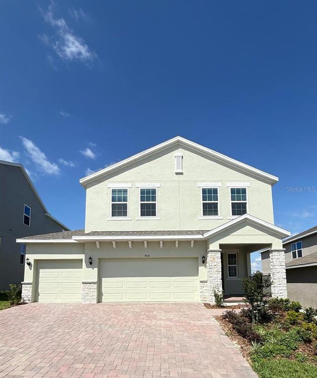 A two-story house with a light-colored stucco exterior, stone accents, and a brick paver driveway — 7501 CATANIA LOOP, CLERMONT, FL