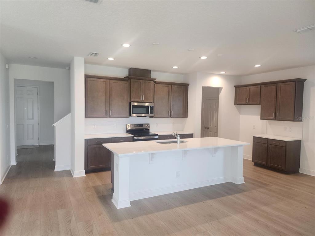 A kitchen features dark wood cabinets, white countertops, a central island, and light wood flooring — 7501 CATANIA LOOP, CLERMONT, FL