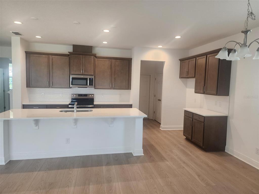 A modern kitchen features dark wood cabinets, white countertops, a center island, and light flooring — 7501 CATANIA LOOP, CLERMONT, FL