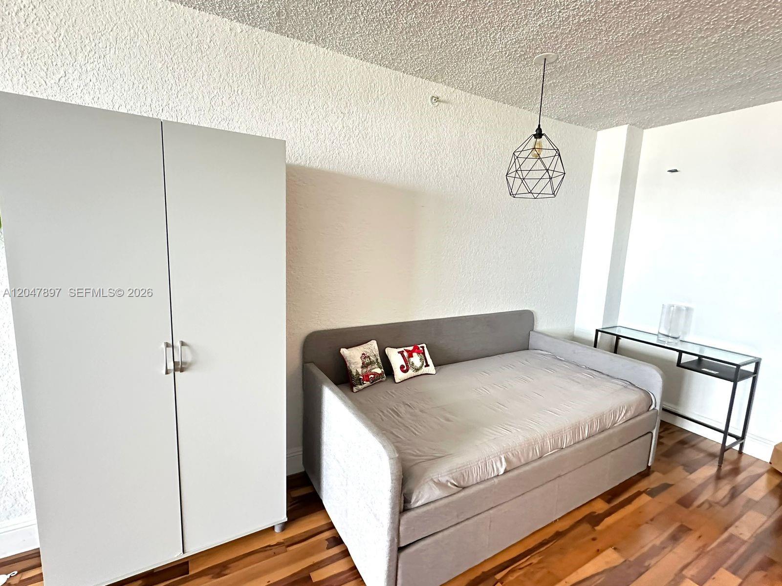 A bedroom features a gray daybed, a white wardrobe, and a geometric pendant light — 1500 Bay Rd # 1408S, Miami Beach FL 33139, MIAMI BEACH, FL